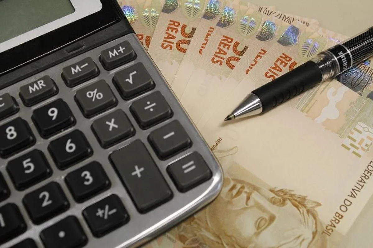 Imagem colorida com calculadora, lapiseira e notas de reais