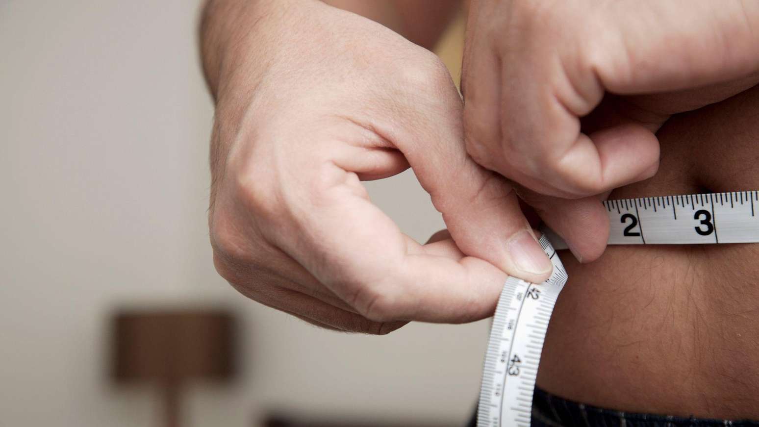 Pessoa mede a barriga com fita métrica.