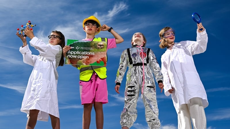 Four young people dressed as scientists pose before a blue sky background
